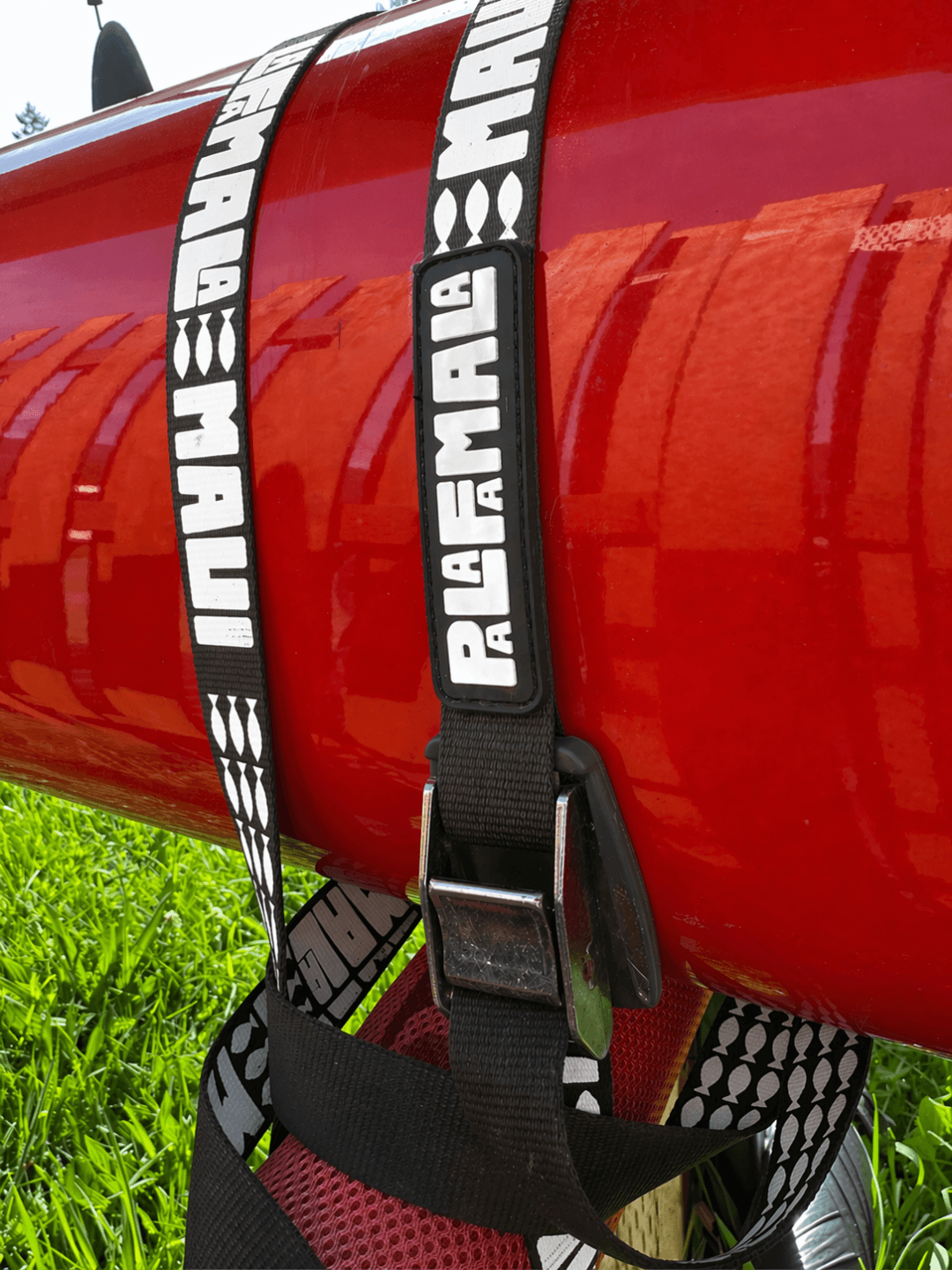Red kayak with a black strap labeled 'PALAFAMALA' on a grassy background