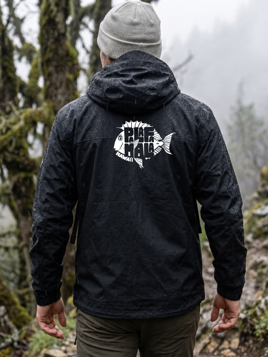 Person wearing a black jacket with a logo on the back, standing in a forested area.