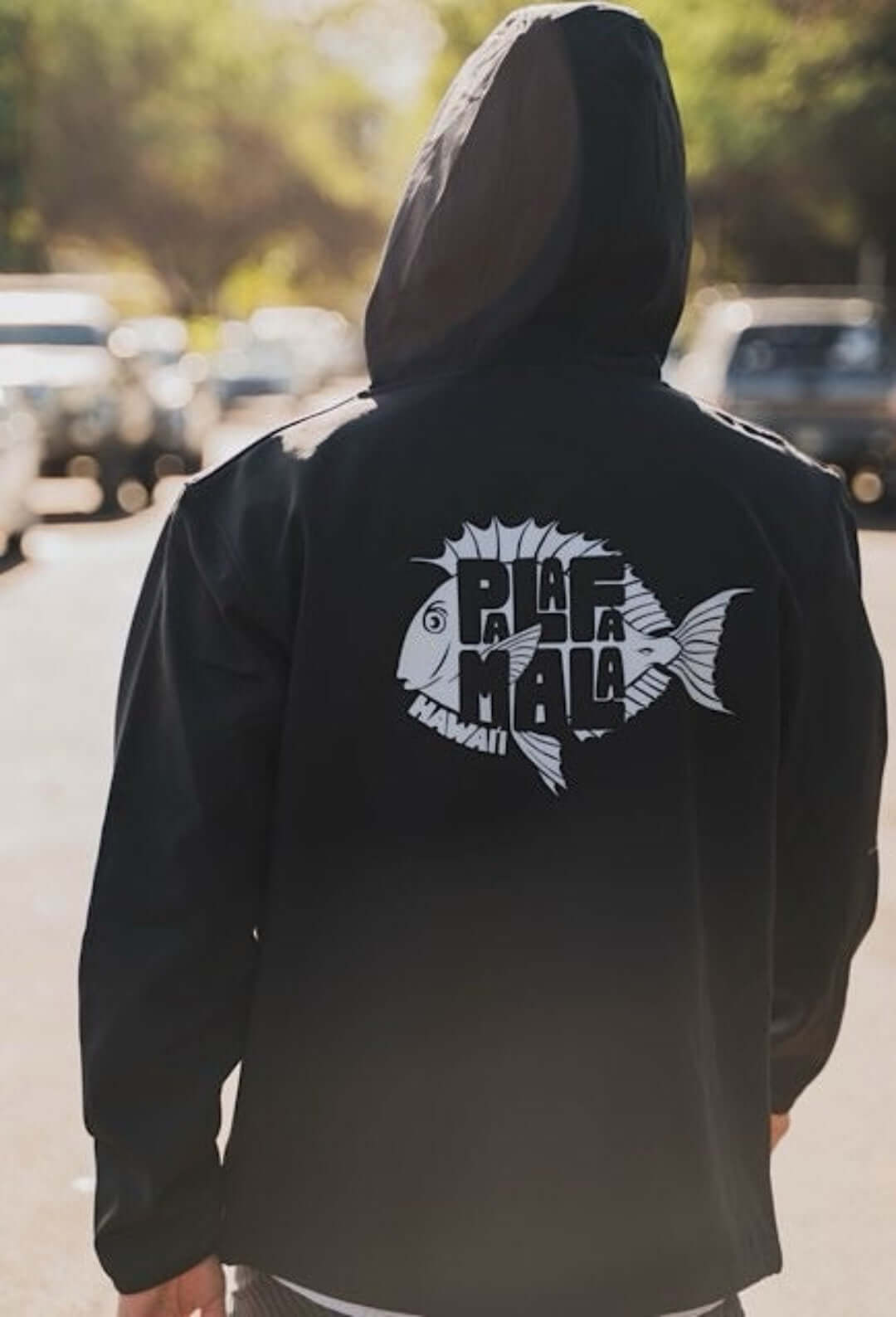 Man in a softshell jacket of PALAFAMALA showing fish logo in a blur street background
